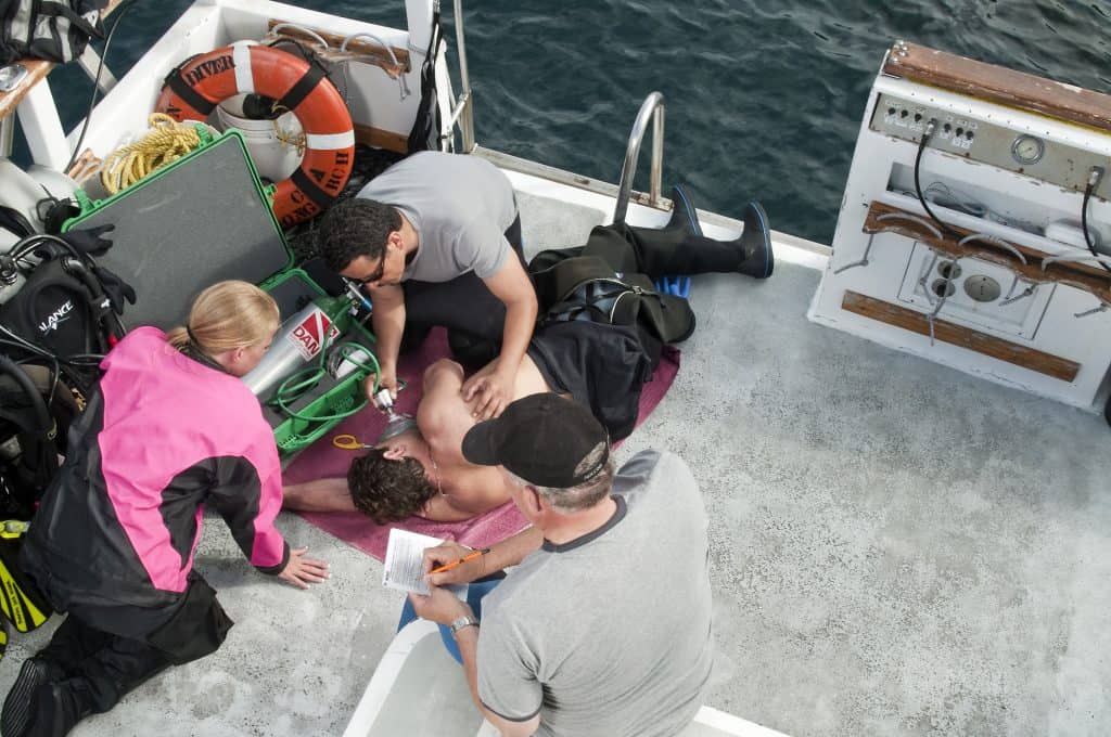 An EFR Instructor overseeing trainees practising an emergency oxygen response scenario on a dive boat
